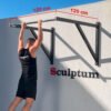 Atleta realizando dominadas en barra de pared Sculptum con gran separación de 120 cm, estructura negra y barra de agarre cromada brillante.